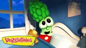 Larry the Cucumber from VeggieTales sits up in bed with a brown teddy bear in a blue bedroom; VeggieTales logo in the corner.