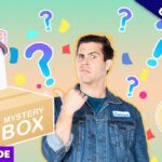 Thumbnail for a mystery box video: man in a denim jacket beside a large 'MYSTERY BOX' with a toaster, guitar, and colorful confetti in the background, 'Exclusive' banner visible.