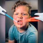 Boy sitting in a chair makes a surprised face as blue and red laser beams pass by his mouth, with white cartoon hands on either side of the image.