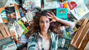 Young woman lies on the floor surrounded by scattered books, notebooks, and school supplies, looking stressed. 125 characters max