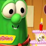 Larry the Cucumber from VeggieTales gazes at a pink birthday cake with a single lit red candle, logo in corner, 25 min badge visible.