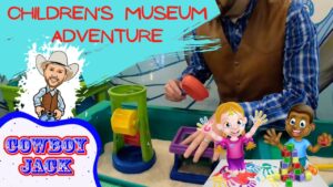 Bright thumbnail for a children's museum adventure: sand play station, a man in a brown vest, cartoon characters, and the text 'Cowboy Jack'.