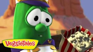 Larry the cucumber from VeggieTales in a captain outfit, looking at a striped popcorn box in a desert landscape.