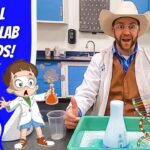 A scientist wearing a cowboy hat and white lab coat leads a kid-friendly science demo at a lab bench, with cartoon characters and a blue banner that reads 'A REAL SCIENCE LAB FOR KIDS!' on the left.