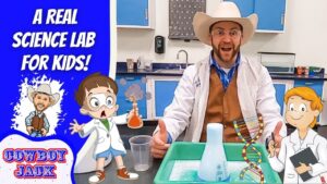 A scientist wearing a cowboy hat and white lab coat leads a kid-friendly science demo at a lab bench, with cartoon characters and a blue banner that reads 'A REAL SCIENCE LAB FOR KIDS!' on the left.