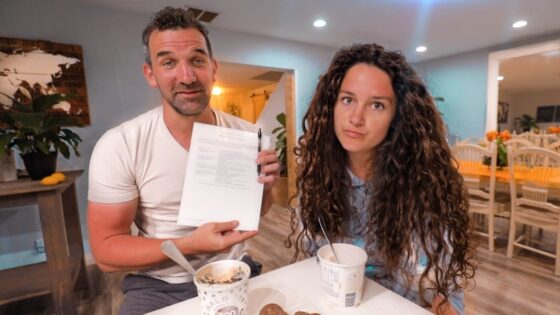 Man and woman at a cafe table with ice cream; the man holds a document and pen toward the camera.