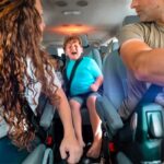 People riding in a minivan; a child in the middle seat is crying while two adults in the front seats drive or interact nearby.
