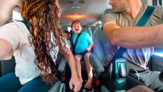 People riding in a minivan; a child in the middle seat is crying while two adults in the front seats drive or interact nearby.