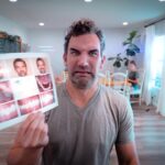 Man grimaces while holding up a dental chart showing teeth photos in a bright room with plants and sitting area in the background.
