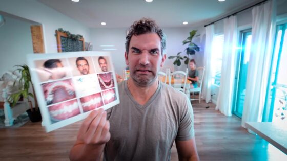 Man grimaces while holding up a dental chart showing teeth photos in a bright room with plants and sitting area in the background.