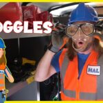 Person in a blue hard hat and orange safety vest wears clear protective goggles inside a workshop; the word 'GOGGLES' is overlaid.