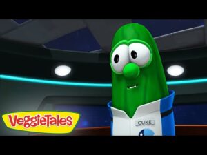 Green cucumber VeggieTales character in a blue-and-white uniform with a 'Cuke' name tag, inside a futuristic control room.