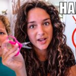 Woman and child watching as the woman cuts a lock of hair with pink scissors; a tangled hair strand is held up in a red circle showing the result.