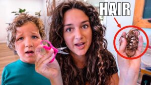 Woman and child watching as the woman cuts a lock of hair with pink scissors; a tangled hair strand is held up in a red circle showing the result.