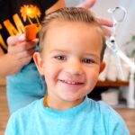 Smiling young boy having his hair styled by a person behind him in a home salon setting.