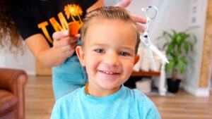 Smiling young boy having his hair styled by a person behind him in a home salon setting.