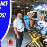 Paramedics pose with a patient on a stretcher beside an ambulance during a kids' ambulance tour event, with a blue panel reading 'Ambulance Tour for Kids' and cartoon cowboy.