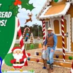 Father and child in cowboy outfits stand beside a giant gingerbread house at a holiday display with large candy canes and festive decorations.