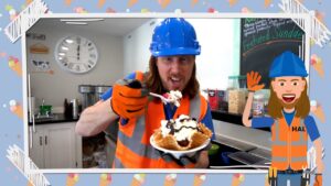 Man in blue hard hat and orange safety vest holds a waffle bowl topped with whipped cream and chocolate sauce in a cafe kitchen; a cartoon construction worker stands on the right.
