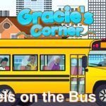 Illustrated yellow school bus with children looking out the windows in a city setting; 'Gracie's Corner' title above and 'Wheels on the Bus' caption.