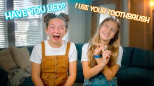 Two smiling girls sitting on a couch, one in tan overalls and the other in denim, with bold captions: 'Have you lied?' and 'I use your toothbrush'.