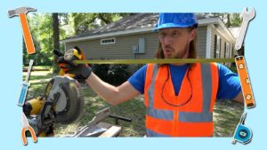 Construction worker in a blue hard hat and orange safety vest holds a level across a miter saw outdoors in front of a house.