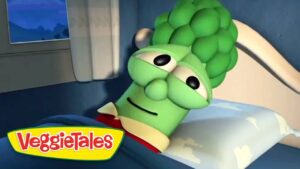 Green VeggieTales character lying in bed with a sleepy expression.