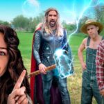 Woman in the foreground points at a Thor-like superhero summoning blue lightning in a rural yard, with two farmers nearby and a wooden barn behind them.