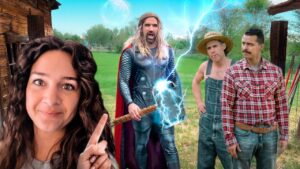 Woman in the foreground points at a Thor-like superhero summoning blue lightning in a rural yard, with two farmers nearby and a wooden barn behind them.