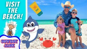 Family with a dad and two kids on a sunny beach, cartoon shark and crab decorations, and a blue 'Visit the Beach!' banner in the background.