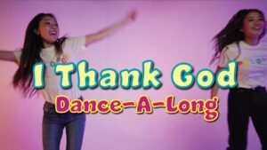 Two girls dancing against a pink backdrop with a bright, colorful title reading 'I Thank God Dance-A-Long' overlaid in the center text.