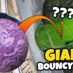 Man in sunglasses grips a massive glittery purple ball at the top of a track, hinting at a giant bouncy ball stunt thumbnail.