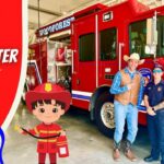 Event at a fire station: a red fire truck with two people posing beside a cartoon cowboy and firefighter stickers in the foreground.