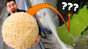 Person at a high ledge holding a giant skein of yarn, eyes wide in surprise, with an orange arc pointing to a distant green valley below.
