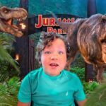 Child posing in front of a Jurassic Park dinosaur display with two roaring T. rex statues behind, jungle backdrop.