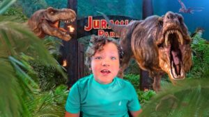 Child posing in front of a Jurassic Park dinosaur display with two roaring T. rex statues behind, jungle backdrop.