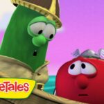 Green cucumber character wearing a hat leans toward a red tomato aboard a wooden ship, with a pink-purple sky and VeggieTales logo in the corner.