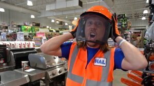 Person in blue shirt and orange safety vest lifts a face shield in a hardware store, with an excited expression.