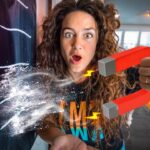 Woman with a red horseshoe magnet sprays chalk dust from a chalkboard in a science demonstration, eyes wide with surprise.