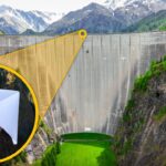 Dam in a mountain valley with a bright yellow magnified circle showing a hand throwing a white paper airplane, highlighting a launch concept.