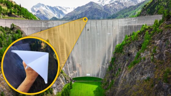 Dam in a mountain valley with a bright yellow magnified circle showing a hand throwing a white paper airplane, highlighting a launch concept.