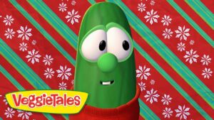 Green VeggieTales character (Bob the Tomato) wearing a red sweater, against a red and teal striped holiday backdrop with snowflakes, VeggieTales logo visible.