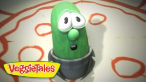 Larry the Cucumber from VeggieTales looks surprised, standing on a circular gray base with a red patterned background and the VeggieTales logo in the corner.