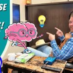 Video thumbnail: a smiling man in a headset sitting in a recliner, pointing at a large cartoon pink brain with glasses and a glowing lightbulb, beside bold ‘EXERCISE OUR BRAINS!’ text and a ‘COWBOY JACK’ logo.