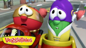 Two colorful VeggieTales characters in a red car, looking surprised as they drive on a city street, with the VeggieTales logo in the corner.