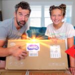 Man and girl unboxing a BenQ package on a living room floor, delighted by the reveal.