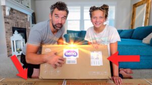 Man and girl unboxing a BenQ package on a living room floor, delighted by the reveal.