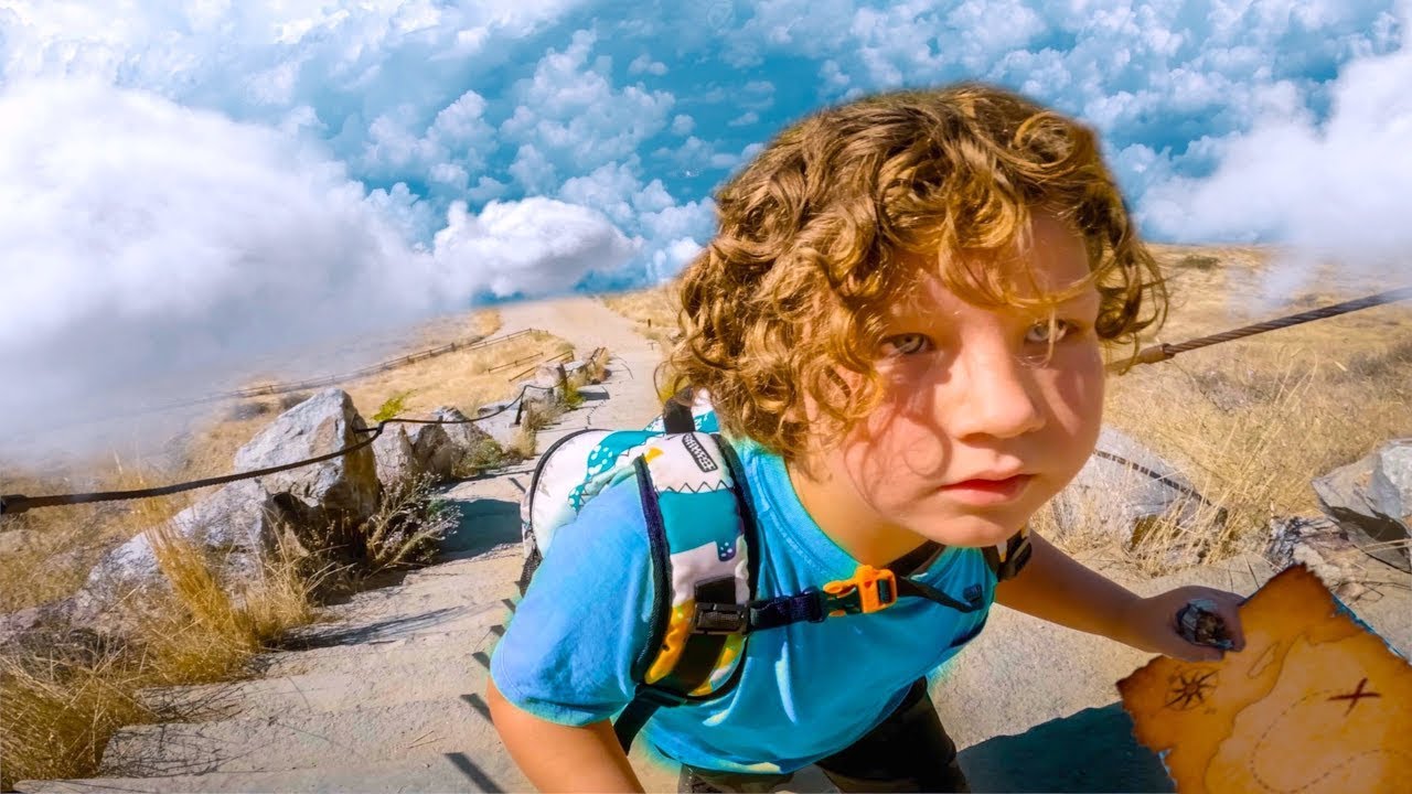 Young child wearing a teal shirt and backpack, on a rocky trail, studying a torn treasure map under a blue sky with clouds.