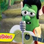 Green VeggieTales character (Larry the Cucumber) sings into a microphone while strumming a guitar; VeggieTales logo visible in the corner.