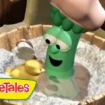 Green VeggieTales character with a smiling face in a wooden tub with white pebbles and a yellow duck nearby, VeggieTales logo bottom left.